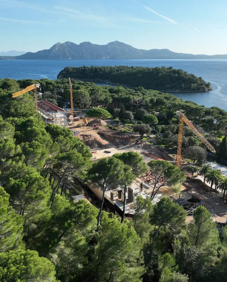 Grúas torre en una obra entre pinos frente a una bahía de Mallorca